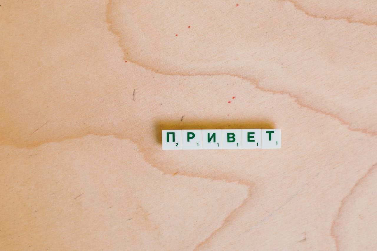Scrabble tiles in Cyrillic spelling 'Hello' on a wooden surface.